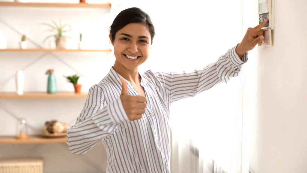 Person giving a thumbs up while adjusting a thermostat